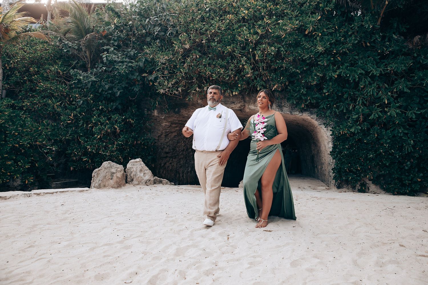 Wedding party posing on white sandy beach surrounded by tropical foliage.