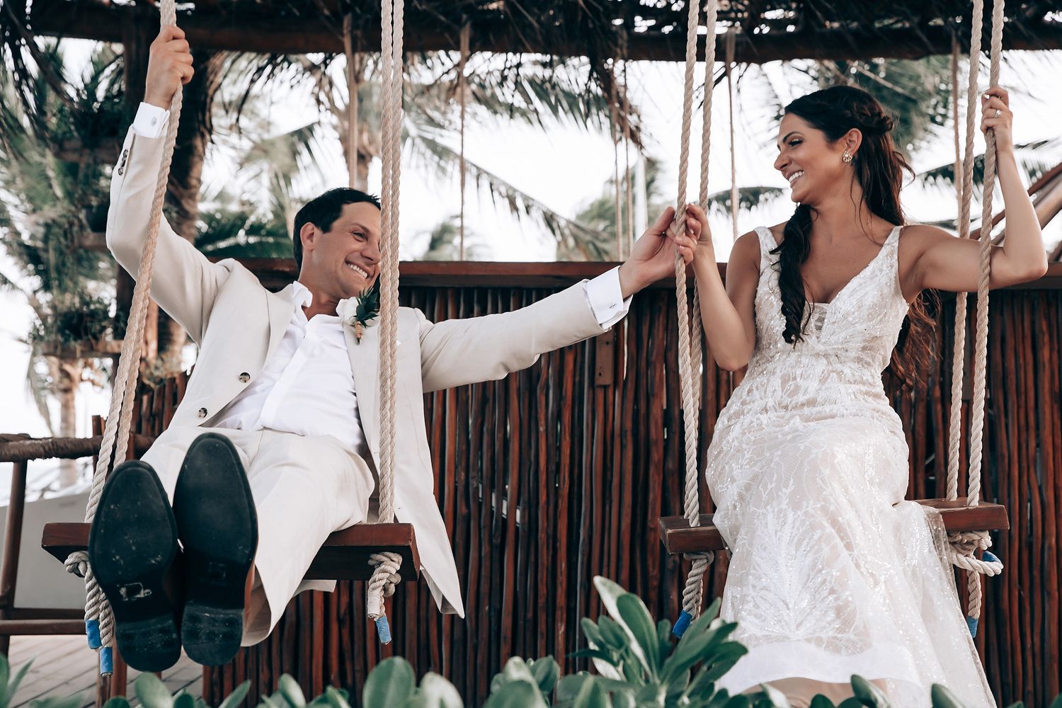 A couple shares romantic moments at a tropical beach wedding venue with palm trees and bamboo decor.