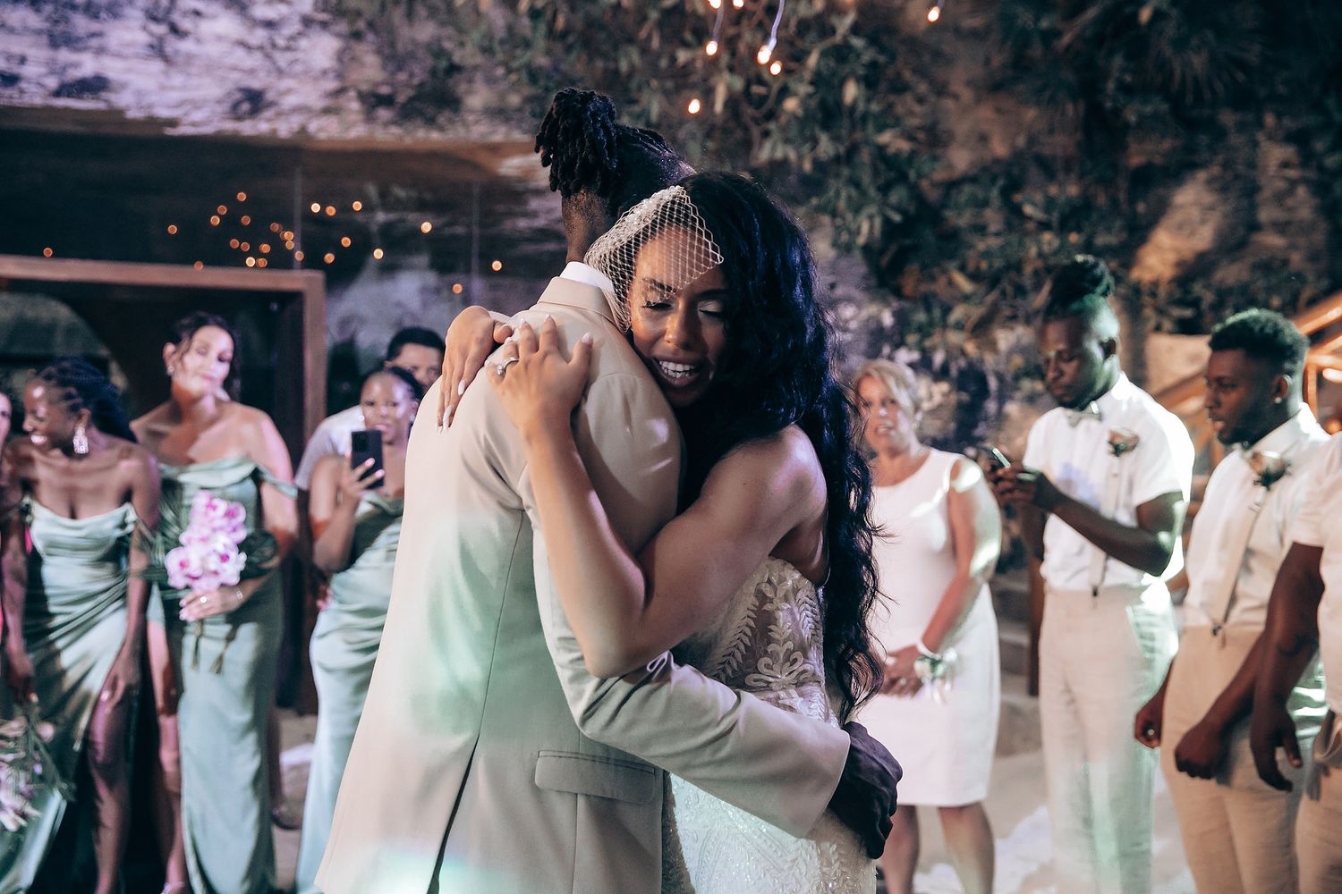 Wedding reception dance moment captured at night with string lights and guests in background.