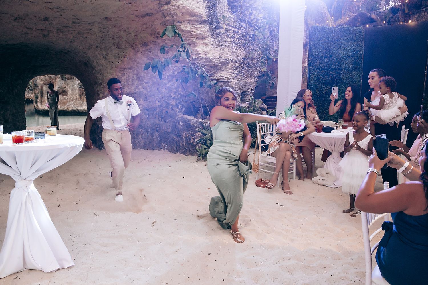 Wedding reception guests dancing and celebrating in a dimly lit cave-like venue.