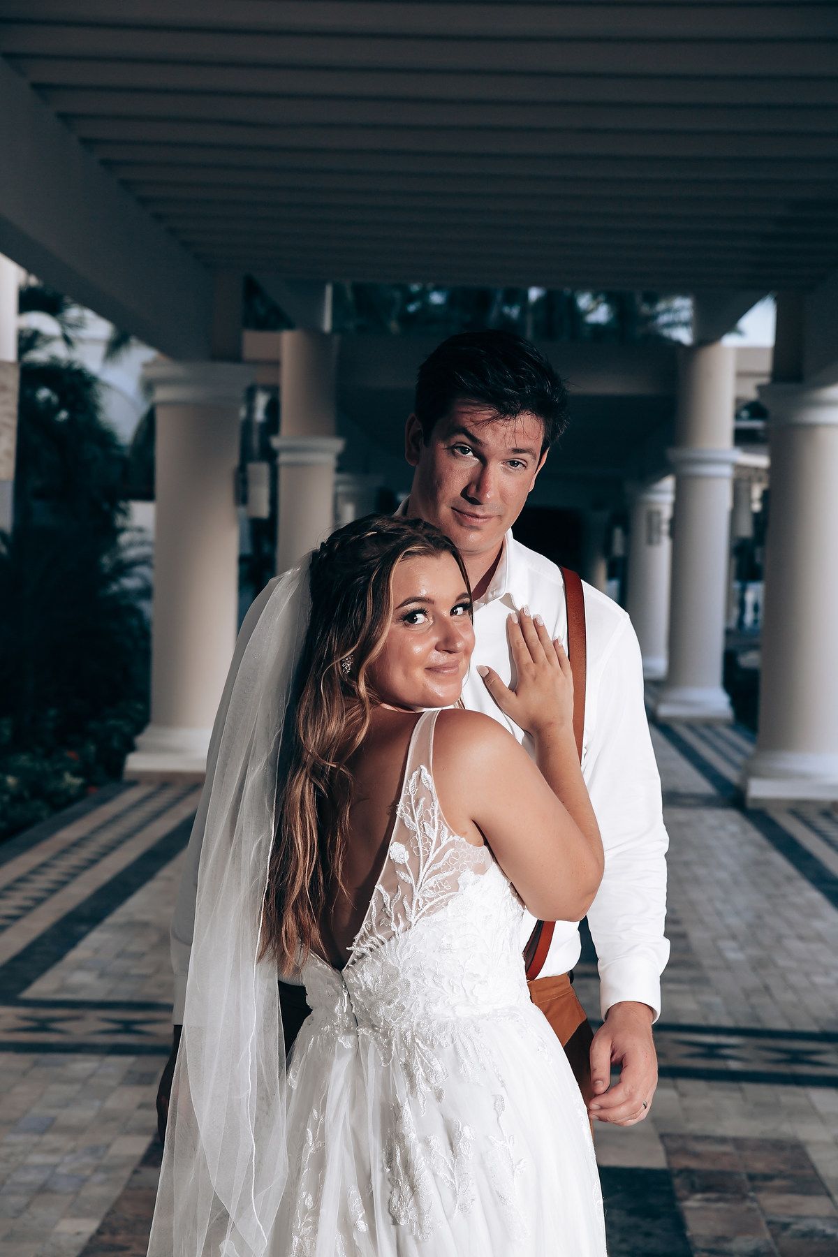Romantic wedding couple shares intimate moment under columned walkway.