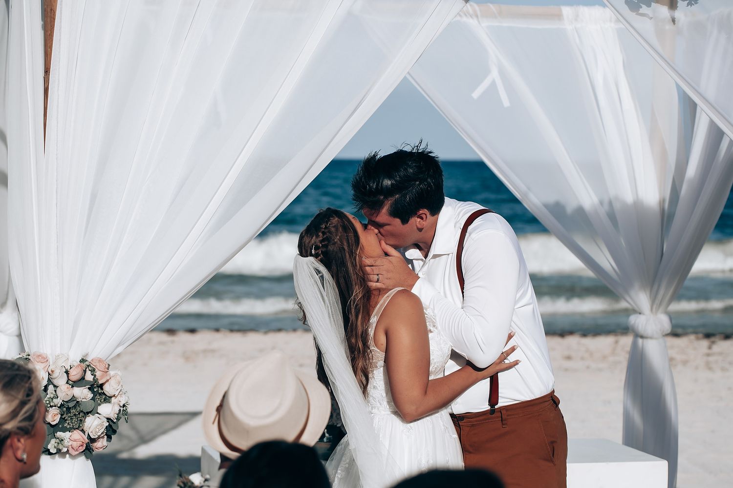 Wedding ceremony under white fabric canopy on tropical beach with ocean view.