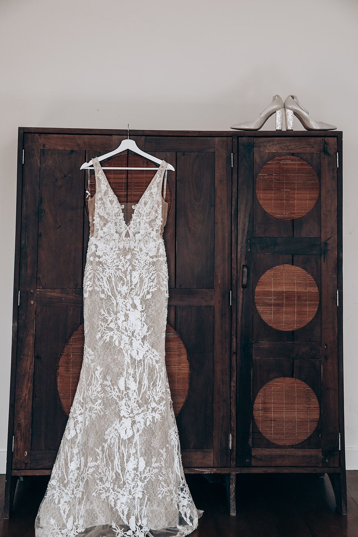 A white lace wedding dress hangs elegantly against dark wooden cabinet doors.