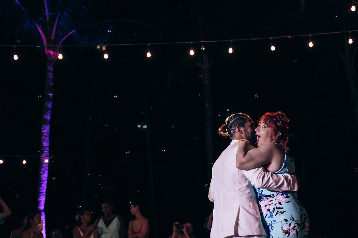 Romantic first dance moment under string lights at nighttime beach wedding reception.