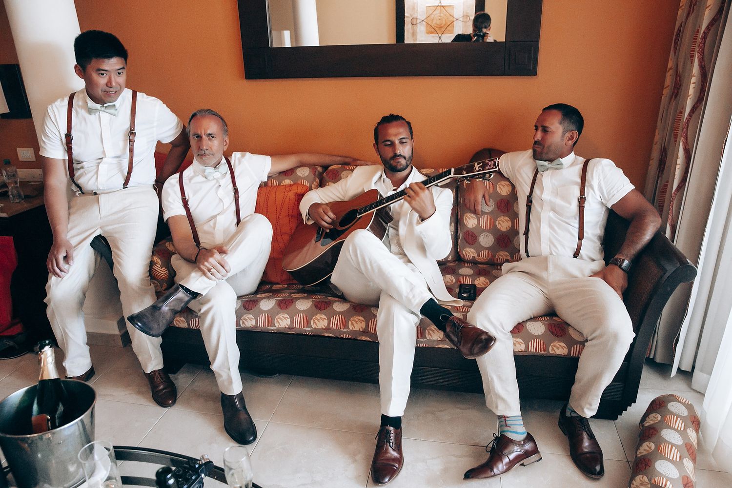 Wedding party in all-white outfits sitting together on a couch for candid group photos.