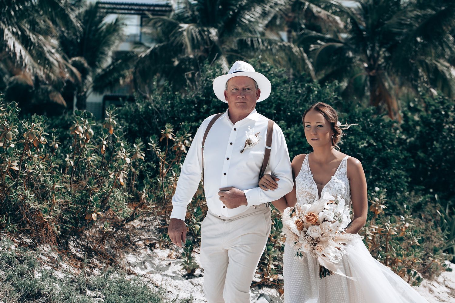 A beach wedding ceremony with attendees dressed in white against a tropical backdrop.