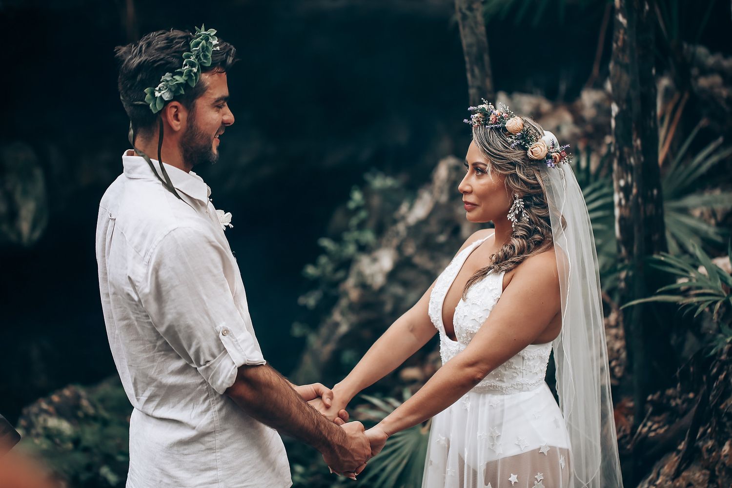 A couple shares an intimate moment during their wedding ceremony surrounded by tropical foliage.