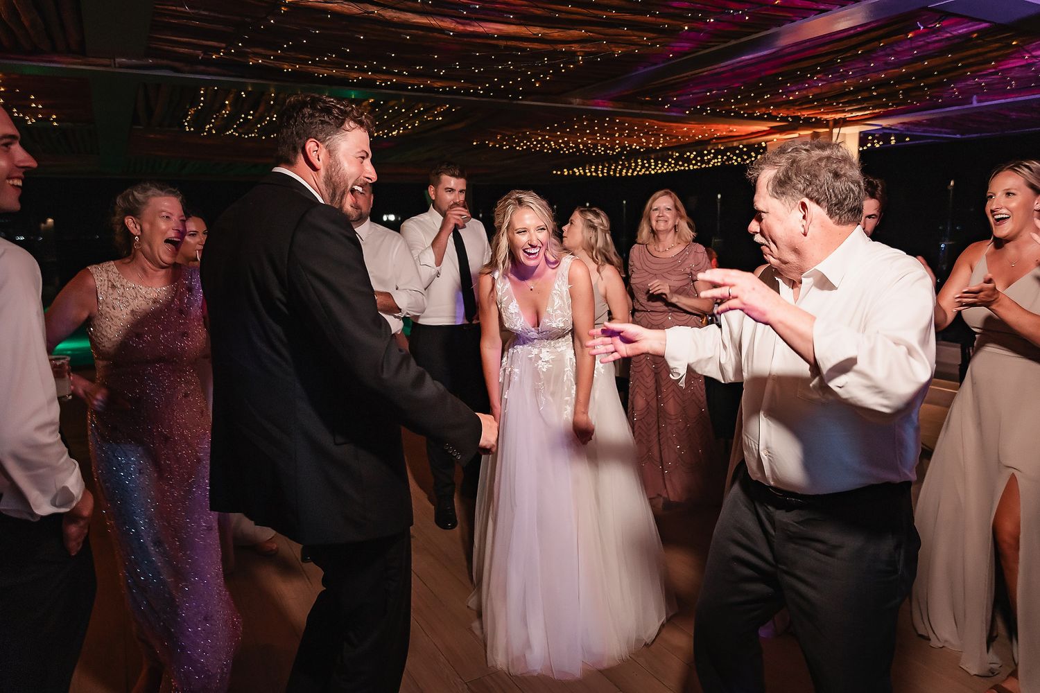 Wedding reception dance party with colorful lighting under a thatched roof venue.