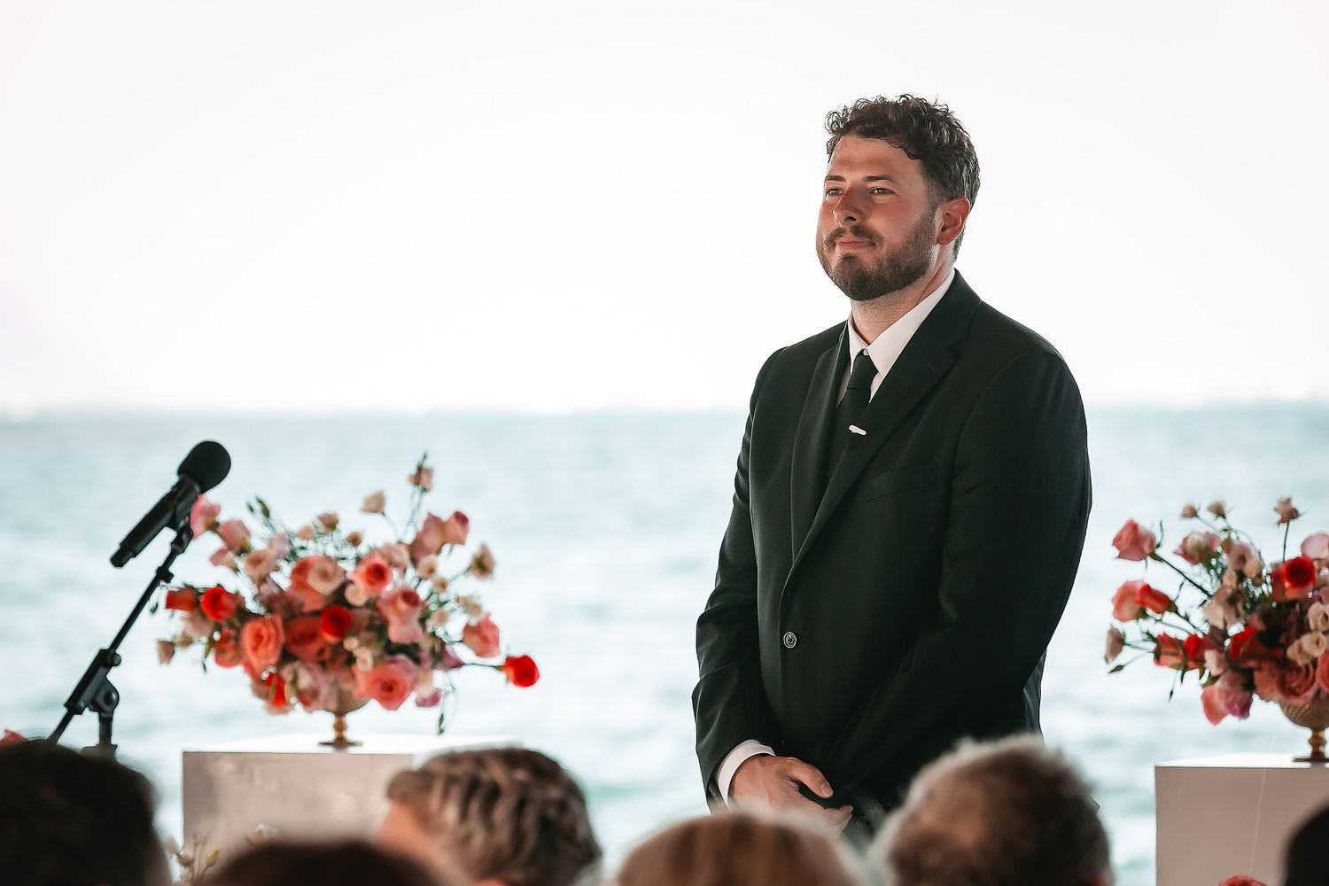 Wedding ceremony setup with ocean backdrop and red floral arrangements.