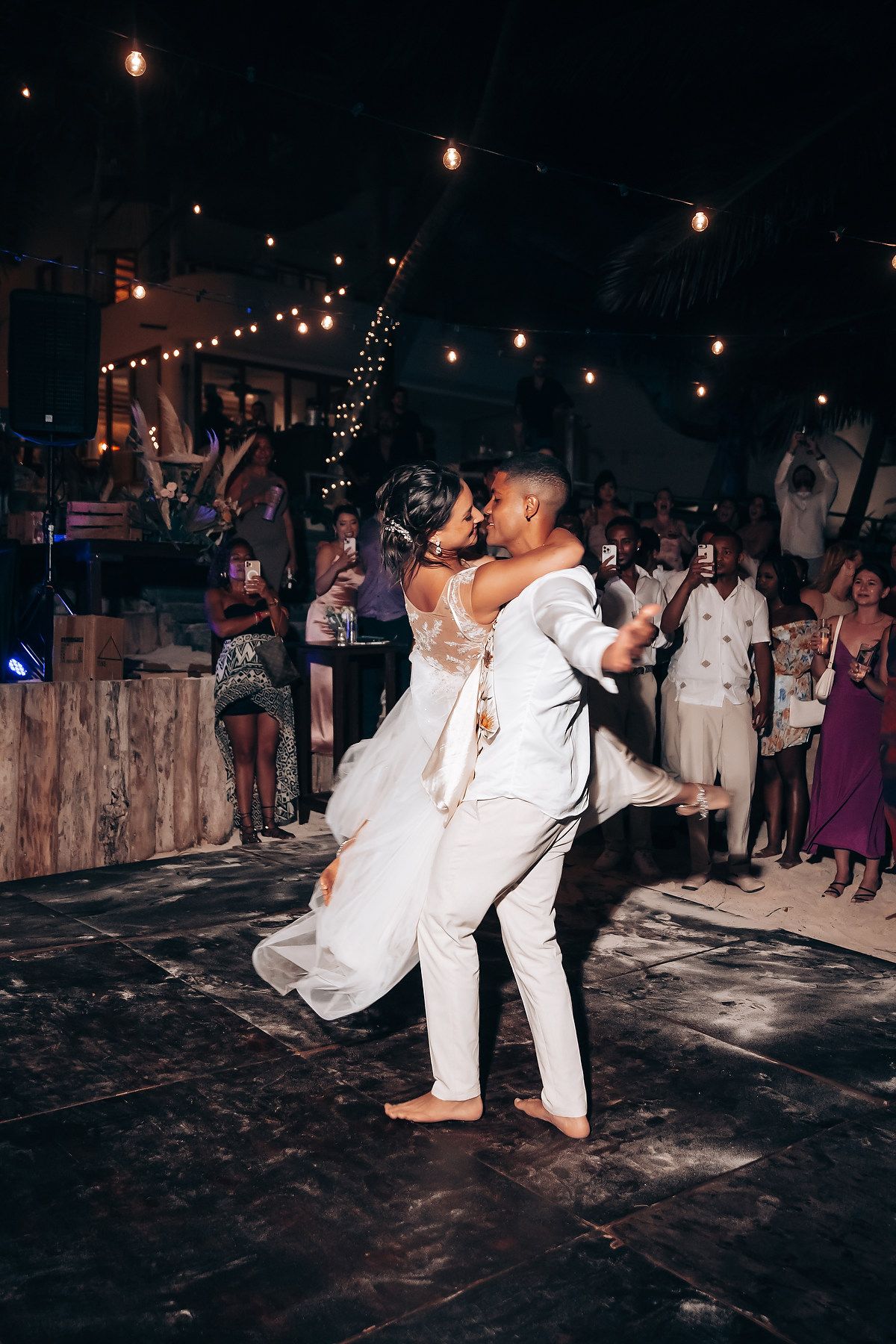 Wedding couple performs a romantic dance dip move on a rustic wooden dance floor under string lights.