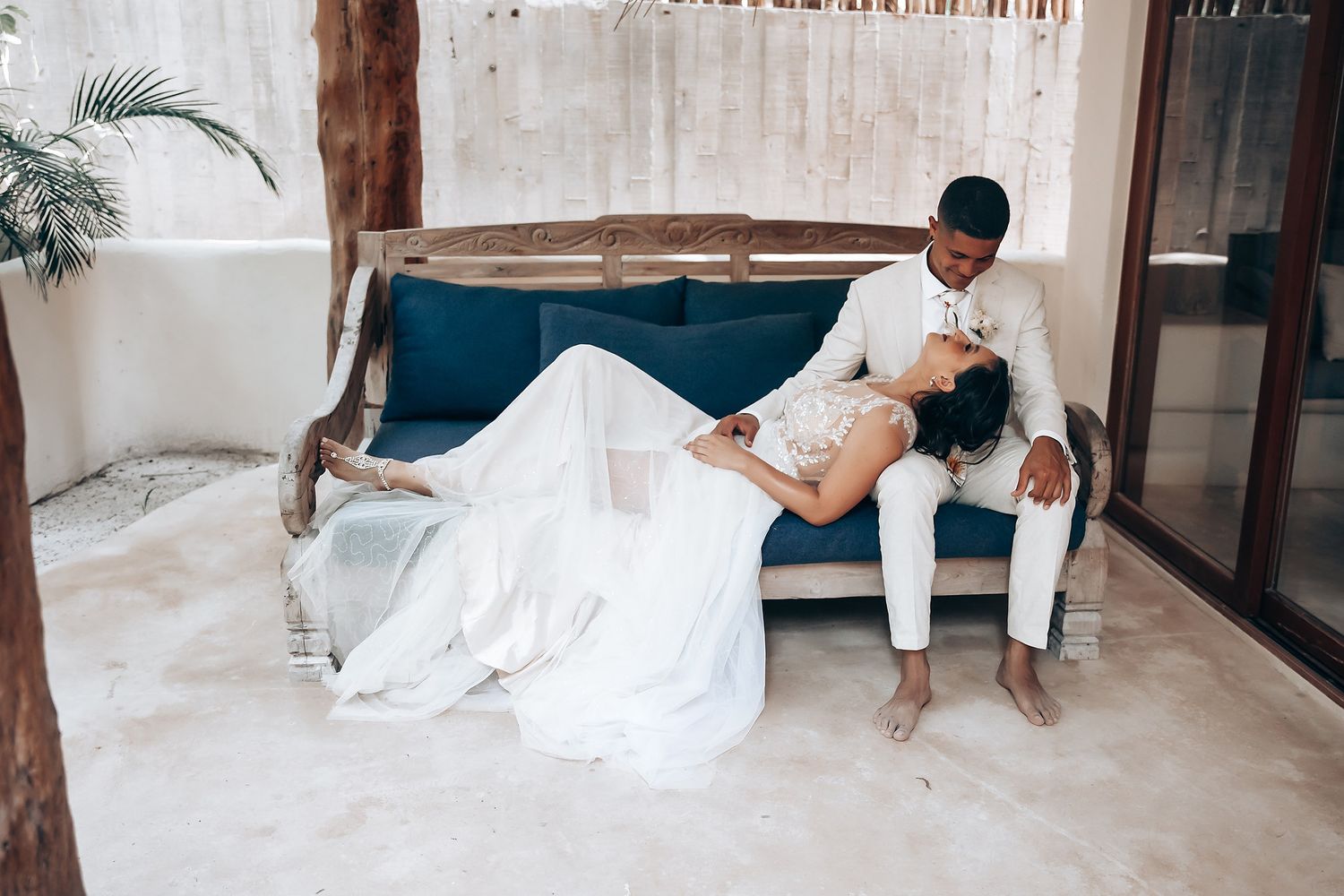 Couple in wedding attire relaxes intimately on blue vintage sofa.