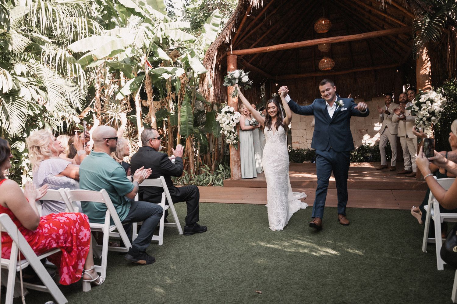 Joyful newlyweds raising hands while celebrating their recessional through cheering wedding guests.
