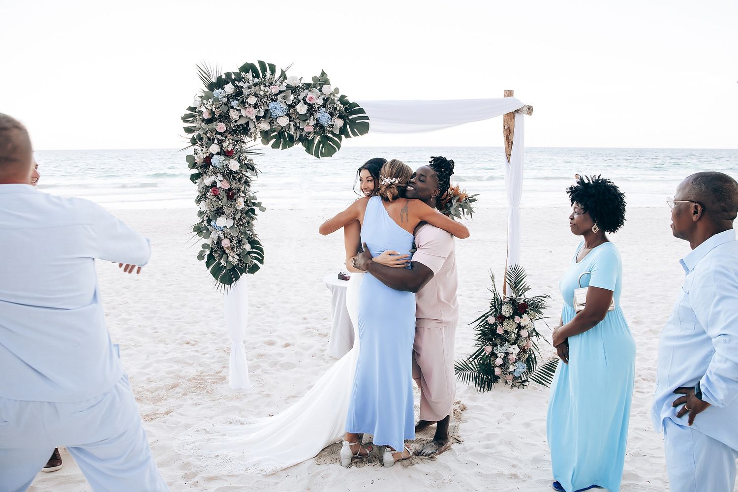 Image of a couple embracing at a beach wedding ceremony with other guests.