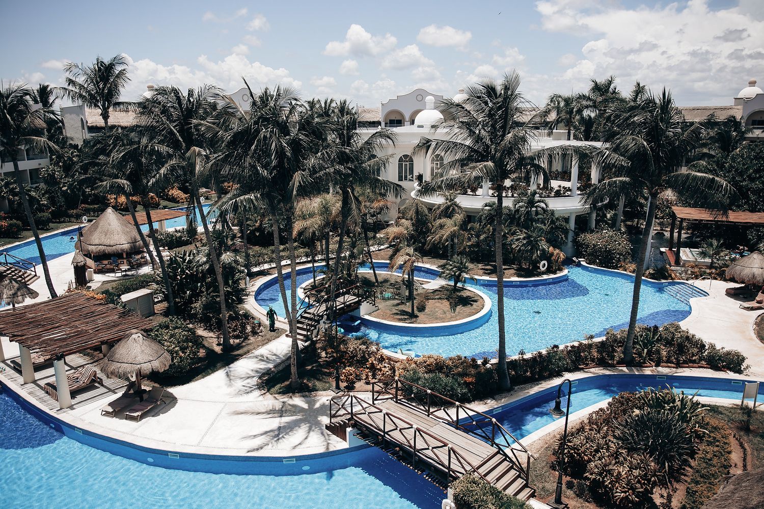 Aerial view of a tropical resort with a large swimming pool surrounded by palm trees and other lush vegetation.