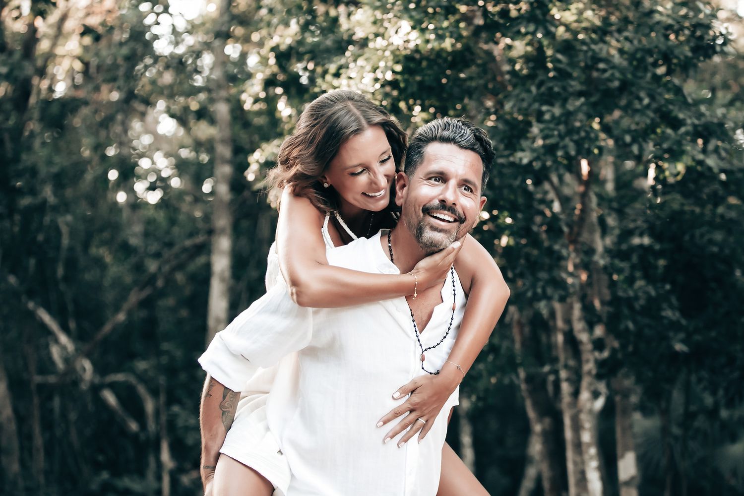 A couple embraces and smiles in a lush, forested landscape.
