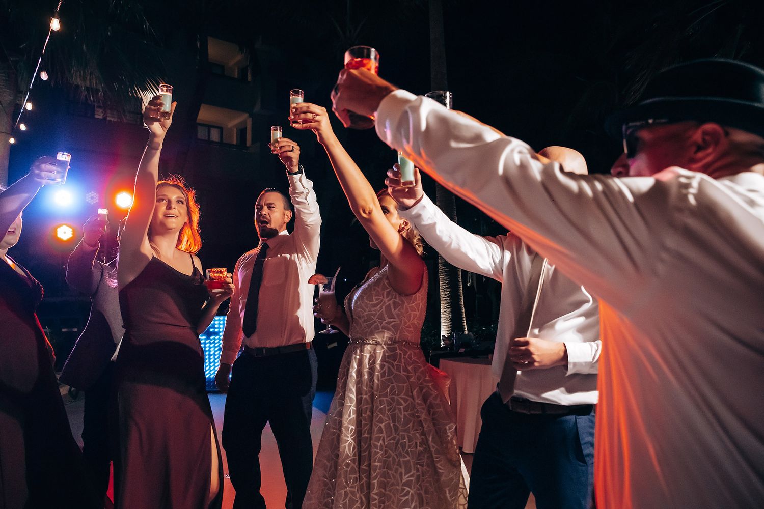 A group of people dancing and celebrating at a lively party or event, with colorful lights and a vibrant atmosphere.