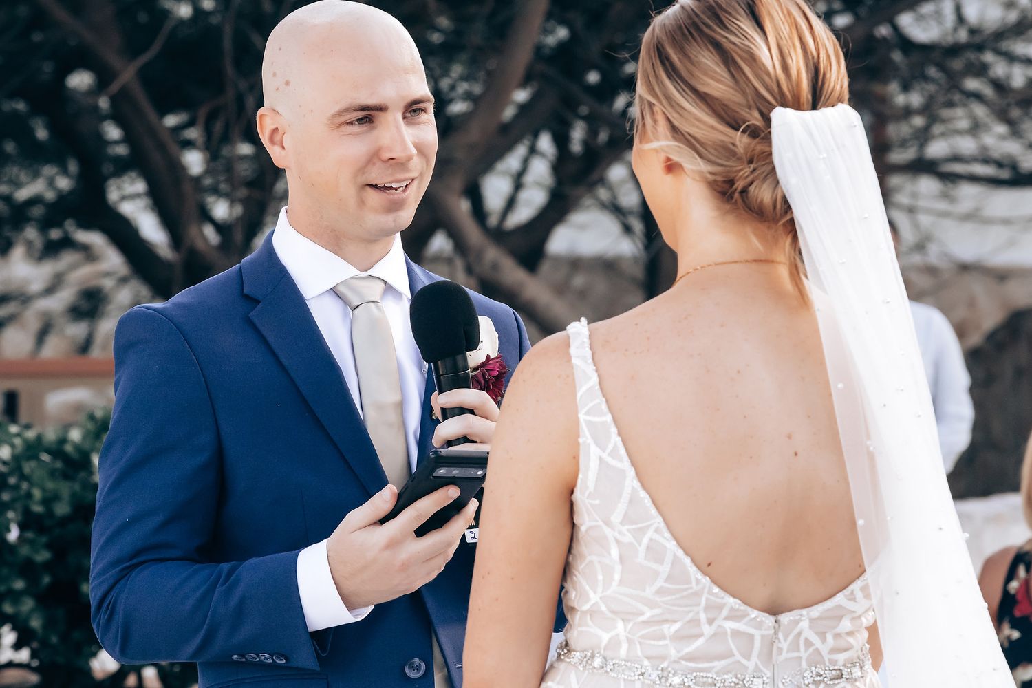 A bride and groom embracing and smiling at each other during their wedding ceremony.