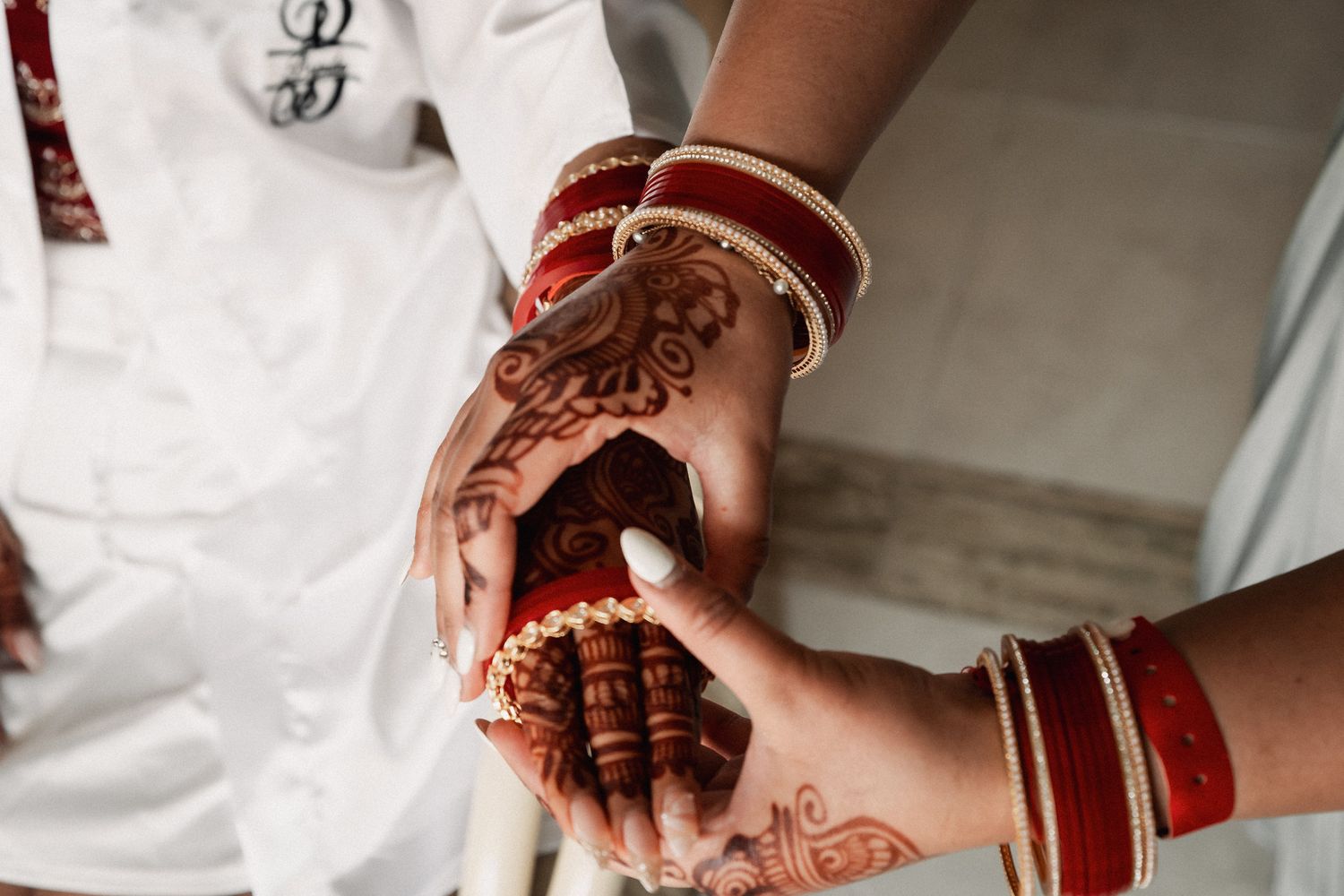 Bride with intricate henna mehndi designs and red gold bangles holding grooms hand at Indian wedding ceremony.
