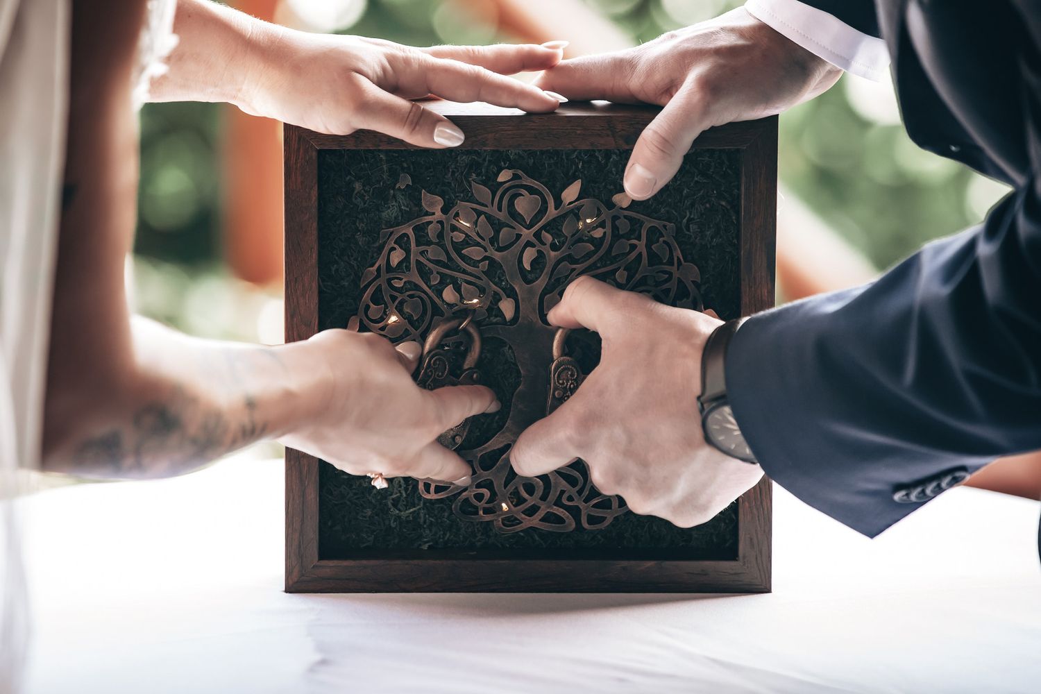 Bride and groom hands touching ornate wooden unity box during wedding ceremony.