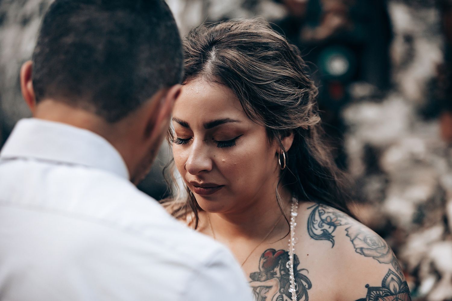 Couple in formal attire sharing an intimate moment in a rustic outdoor setting.