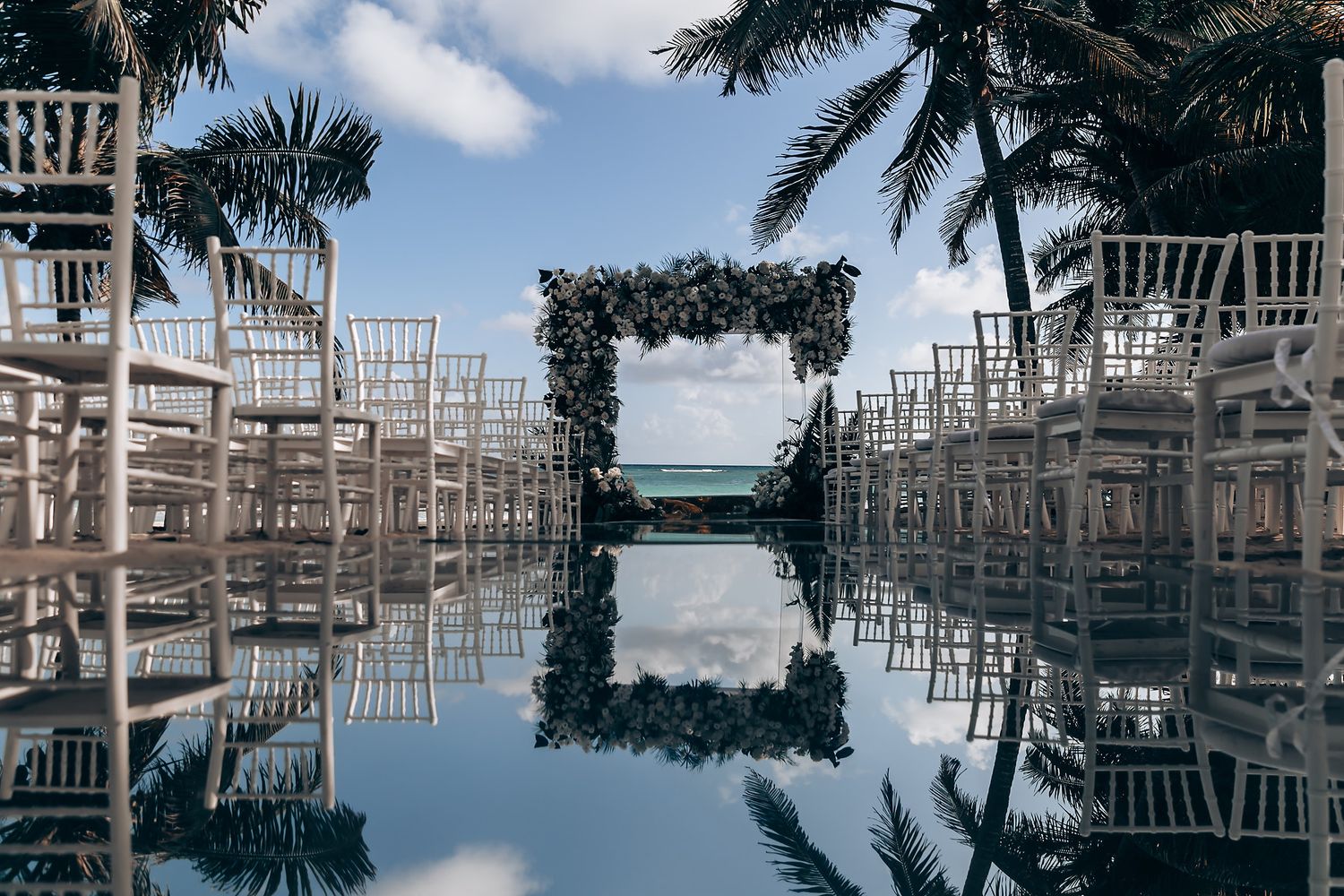 White chairs arranged for an outdoor wedding ceremony with palm trees and ocean views.