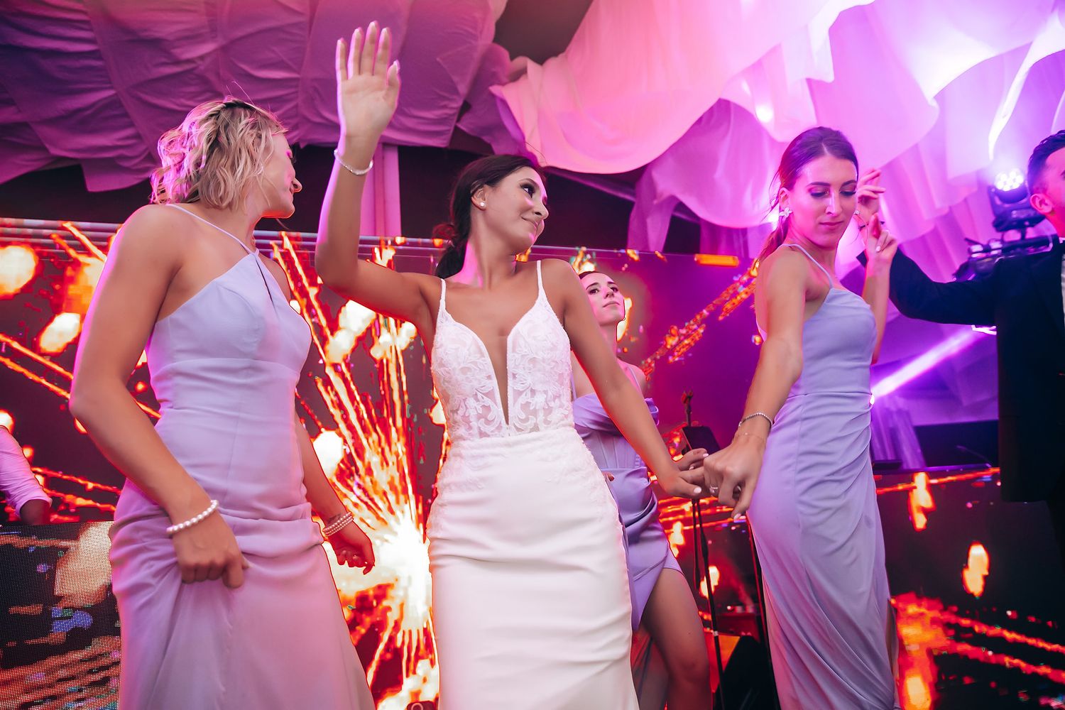 Wedding reception dance floor illuminated with pink and purple lighting as guests celebrate.