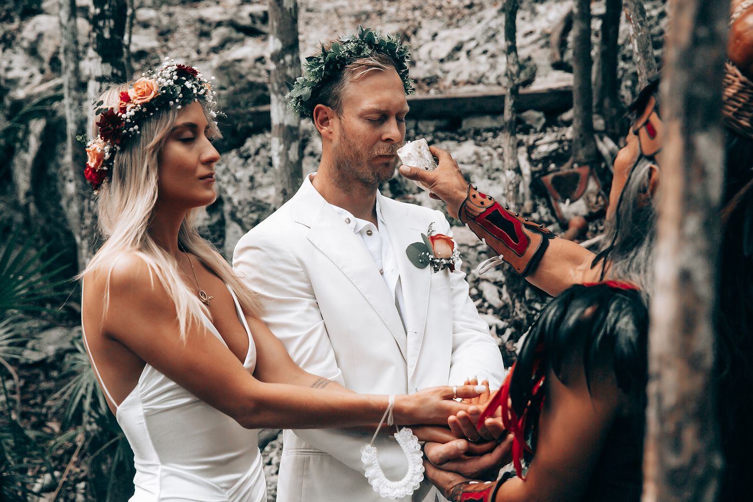 Wedding ceremony participants bind hands with colorful ribbons during outdoor forest ritual.