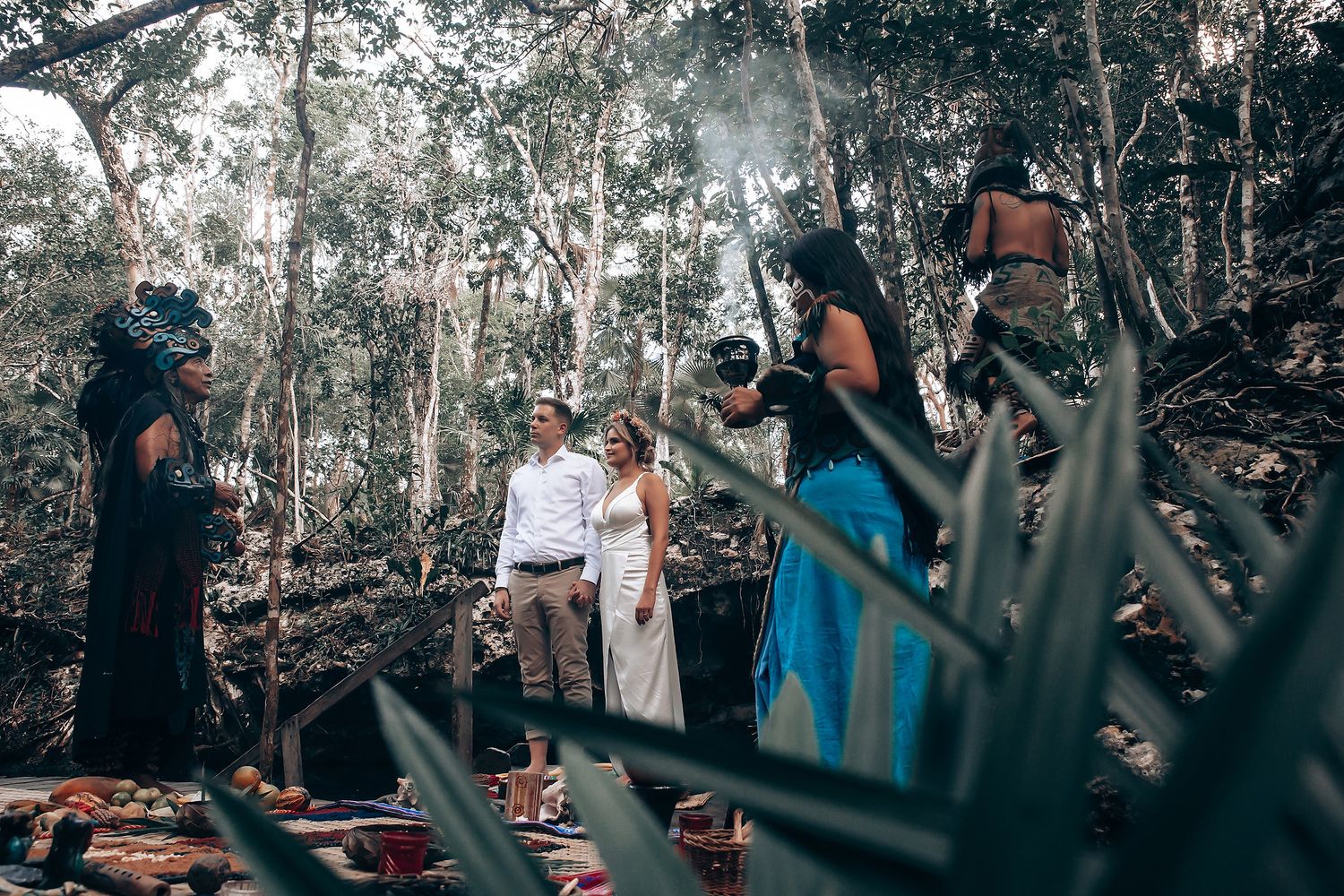 A couple poses for a wedding photoshoot in a lush tropical forest setting with photographers in the background.