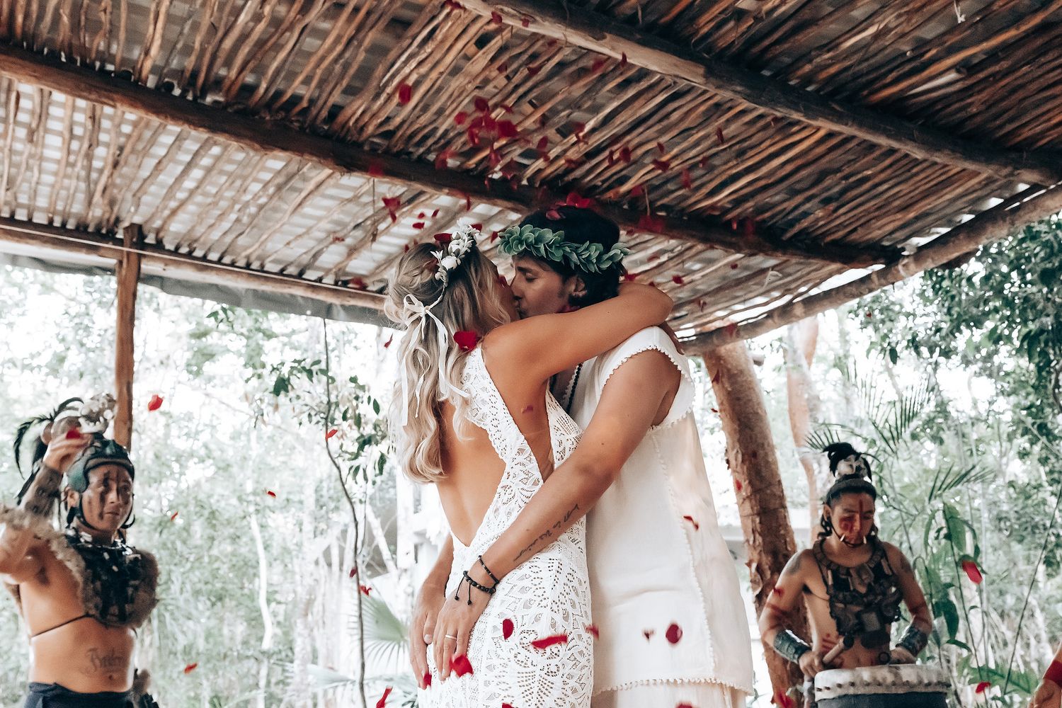 Romantic outdoor wedding ceremony under a rustic wooden canopy with floral decorations and white dress.