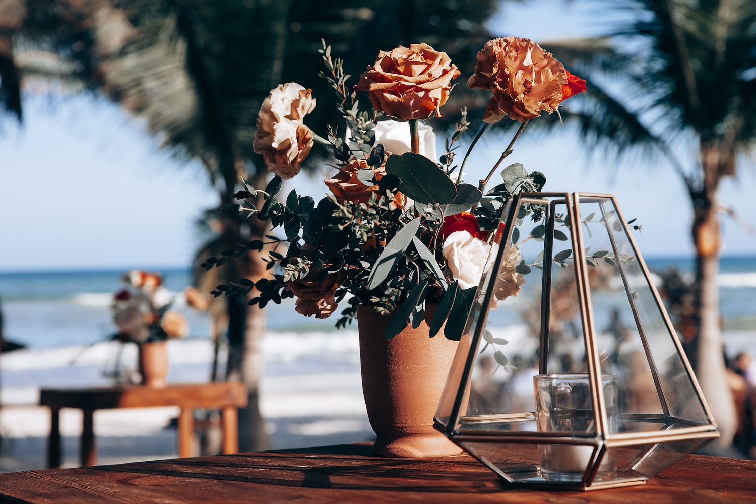 Rustic beachside wedding setup with dried floral arrangements and palm trees against an ocean backdrop.
