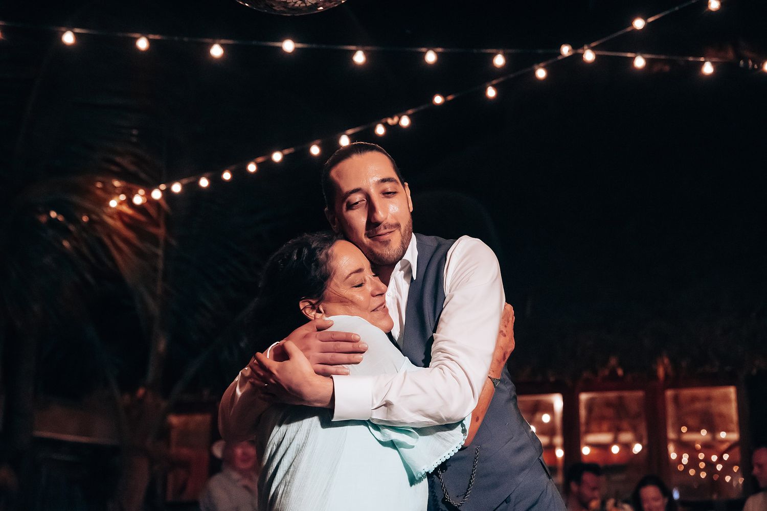 Romantic dance moments captured under twinkling lights at a beach wedding reception.