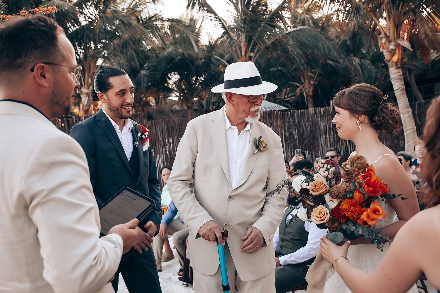 Wedding guests gathered outdoors under palm trees during a beachside celebration.