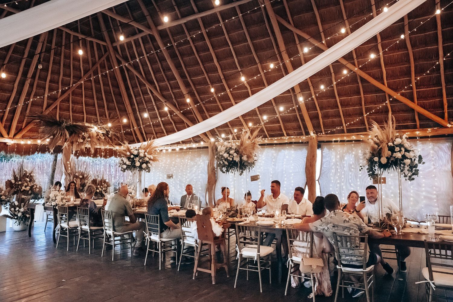 A rustic barn wedding reception venue with exposed wooden beams, white drapes, and elegant table settings.