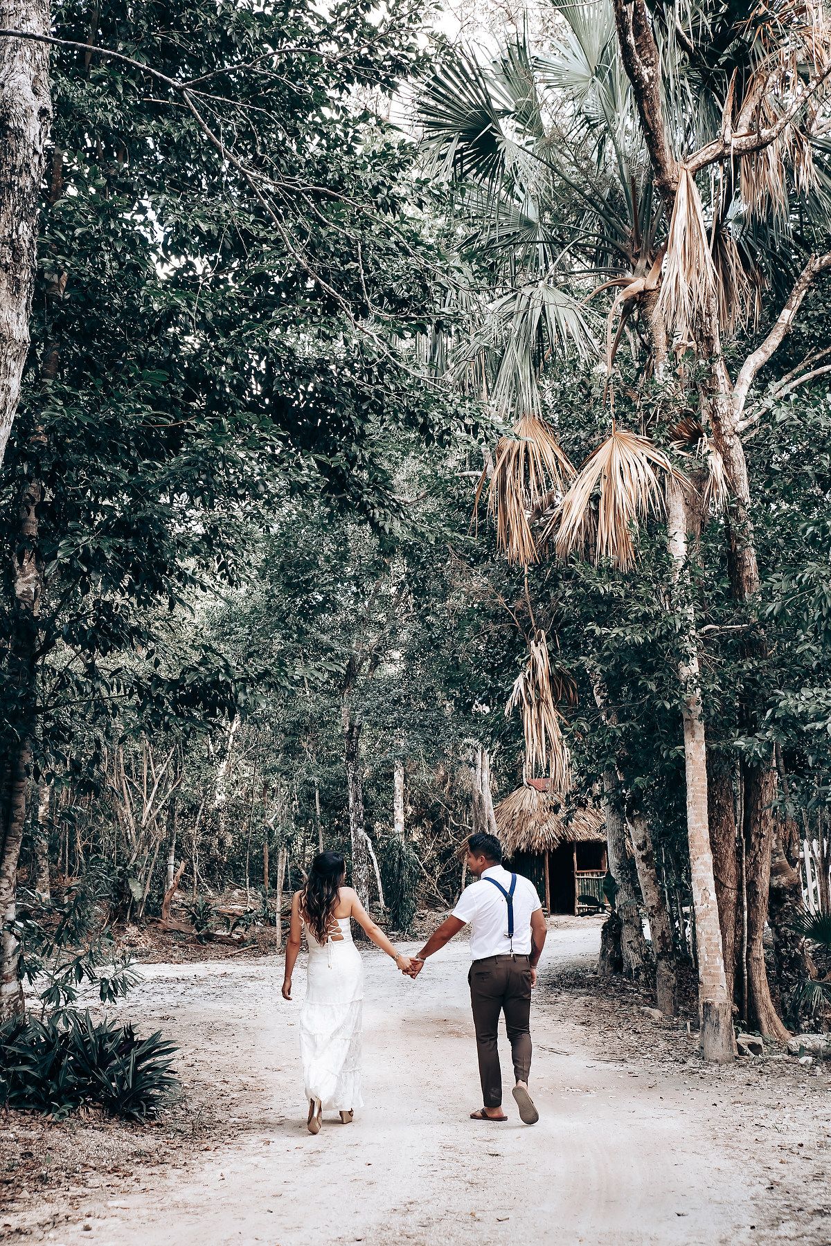 A panoramic view of a wooded path with palm trees and figures walking along a sandy trail.