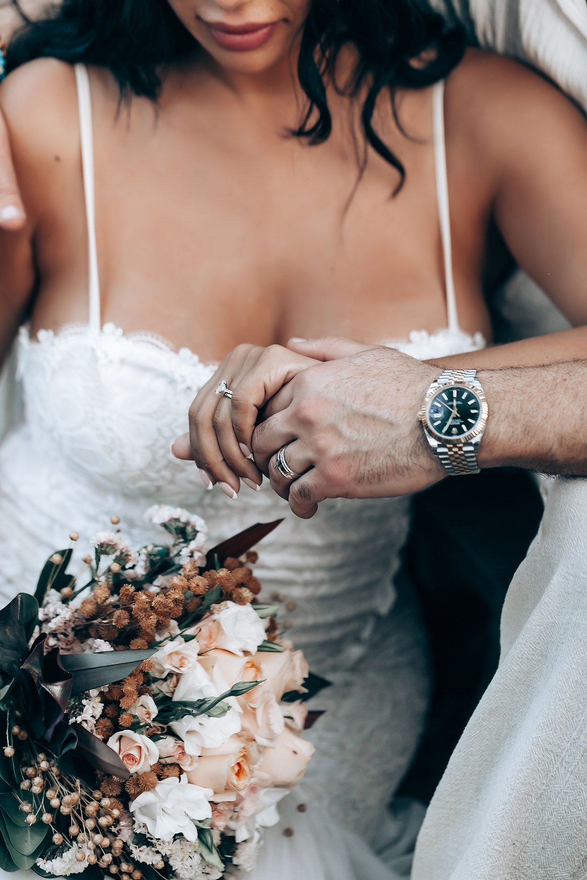Close-up detail of hands holding wedding bouquet with delicate flowers and jewelry.