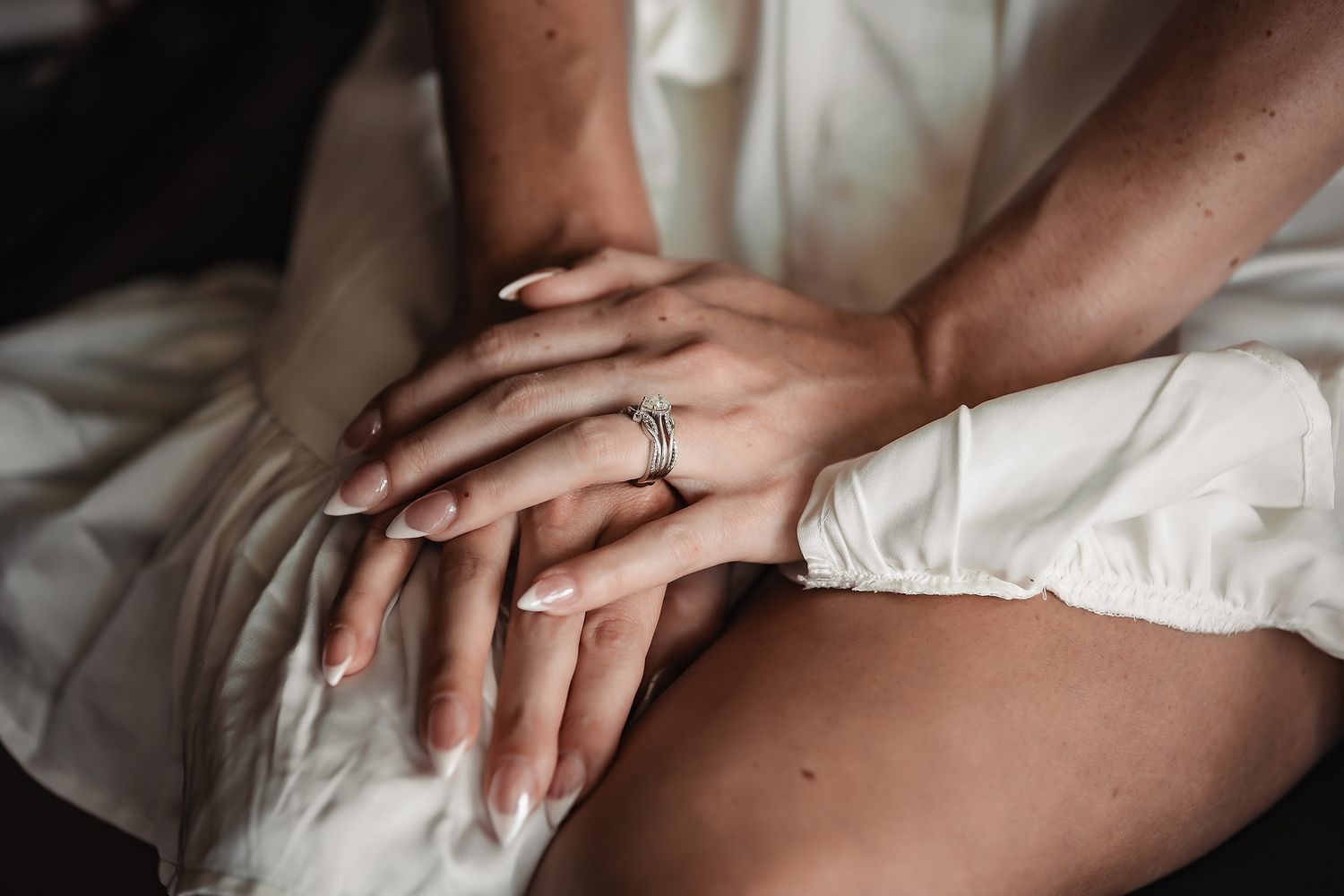 Close-up of bride's hands showing diamond engagement ring and manicured nails.