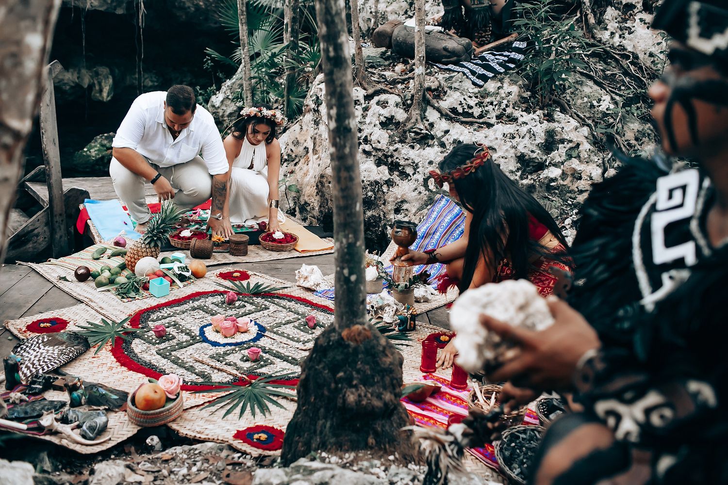 Ceremonial gathering with participants seated on woven mats in a natural setting.