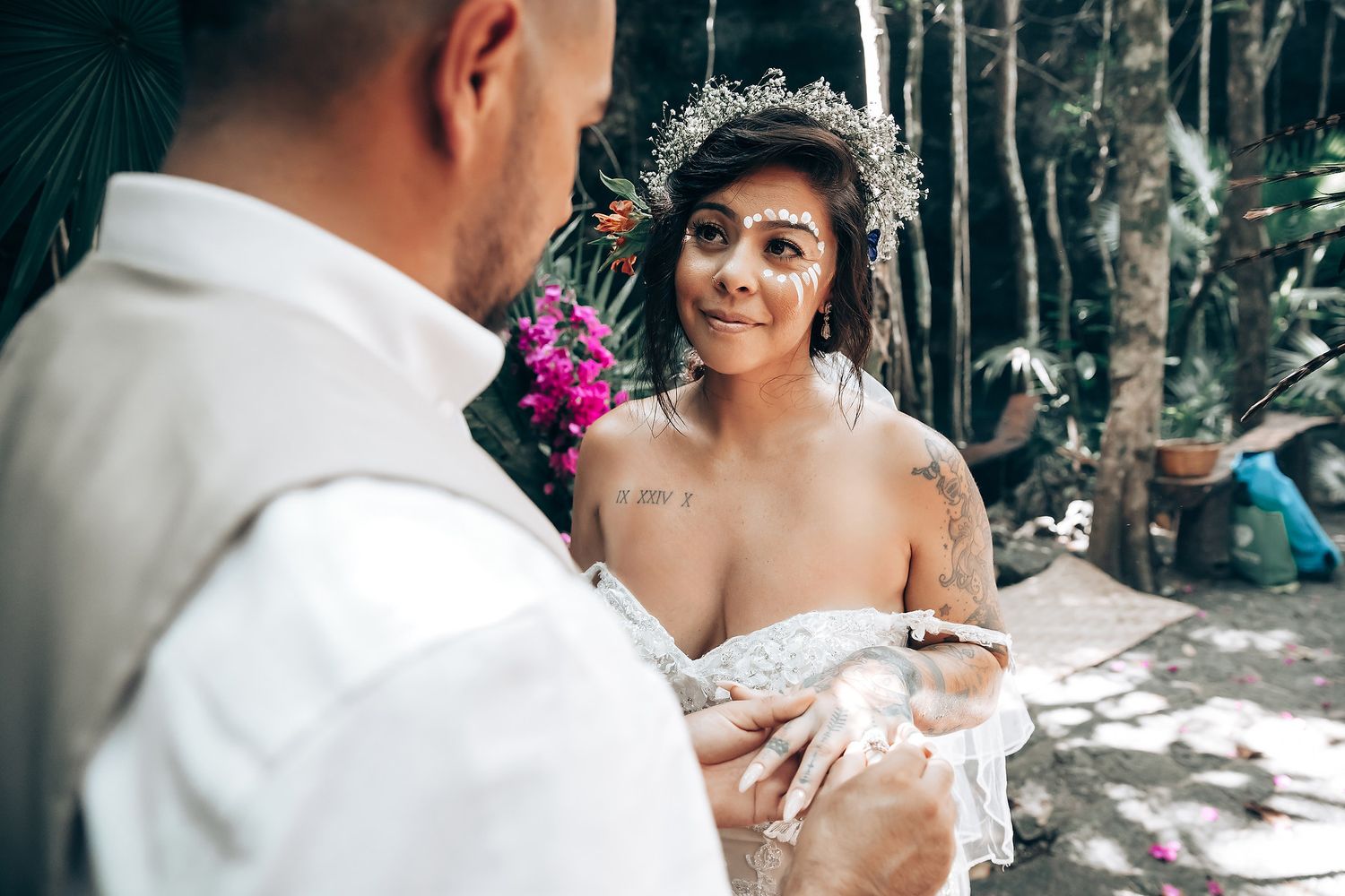 Wedding ceremony participants gather in a lush forest setting with dappled sunlight.