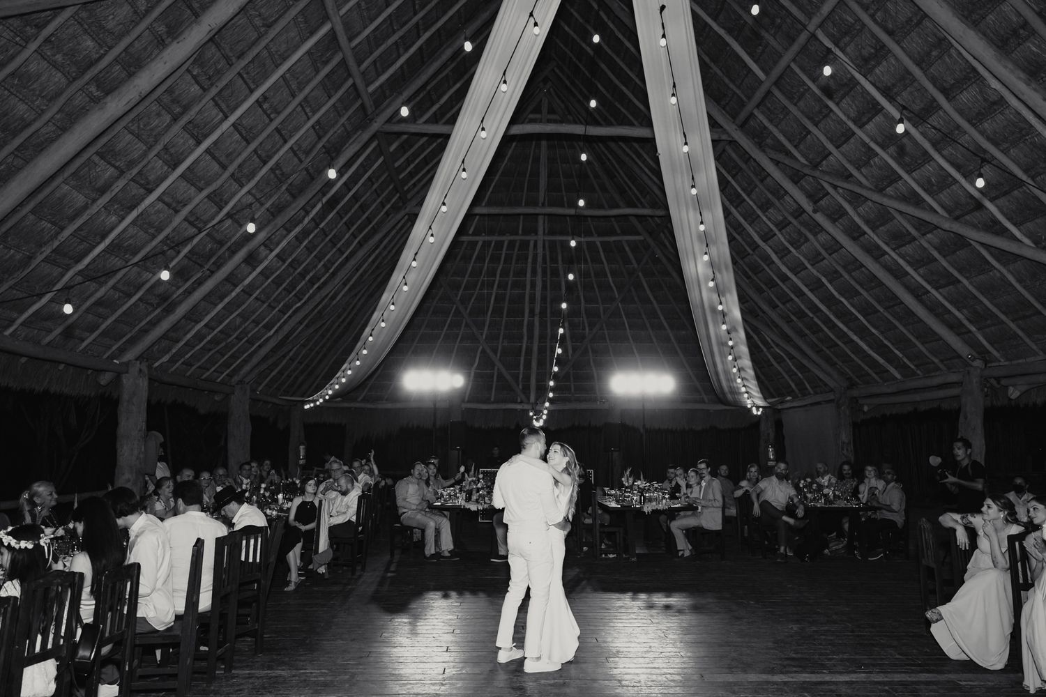 Black and white photo of bride and groom sharing their first dance in a grand open-air reception hall.