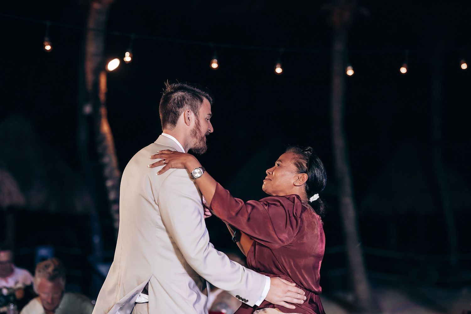 Romantic dance moment under twinkling lights at an evening wedding reception.
