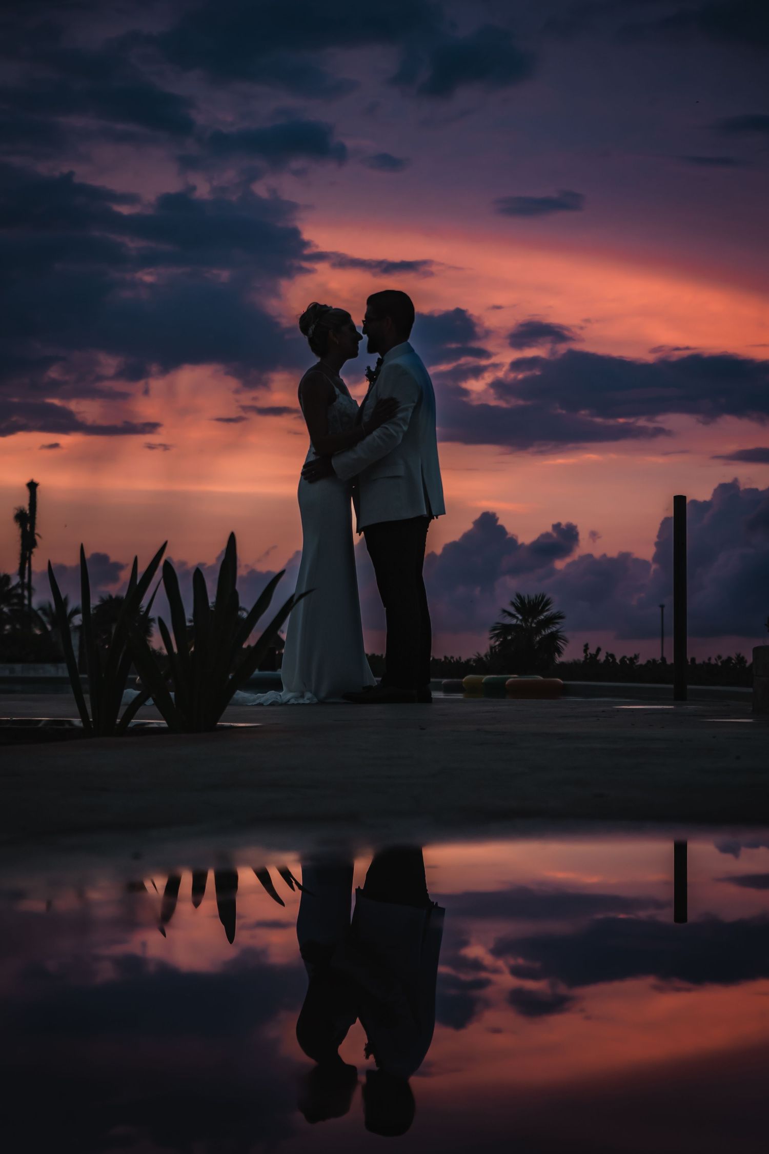 Dramatic silhouette reflection of wedding couple in water during purple sunset.