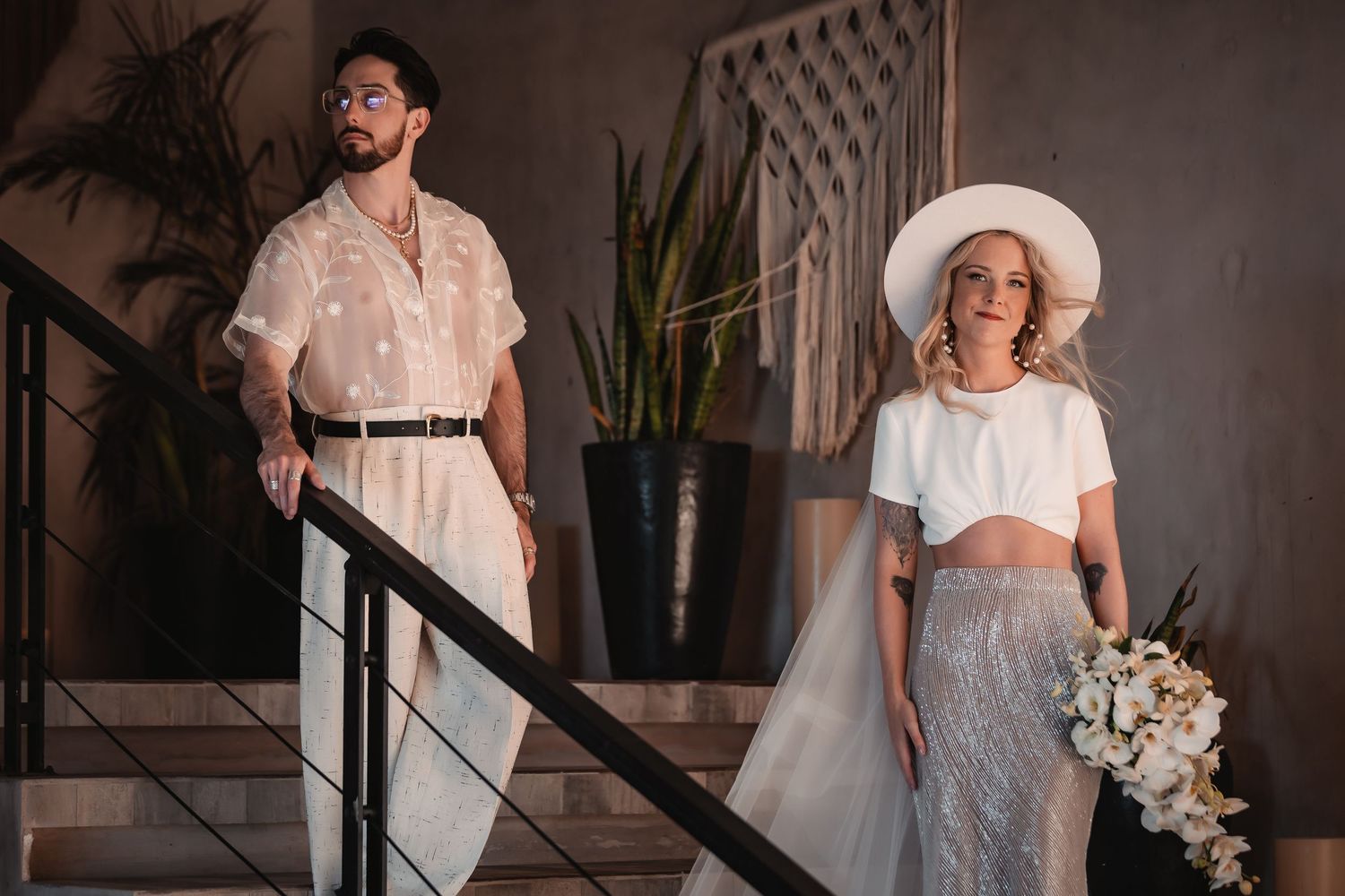Couple in white outfits posing on modern concrete stairs.
