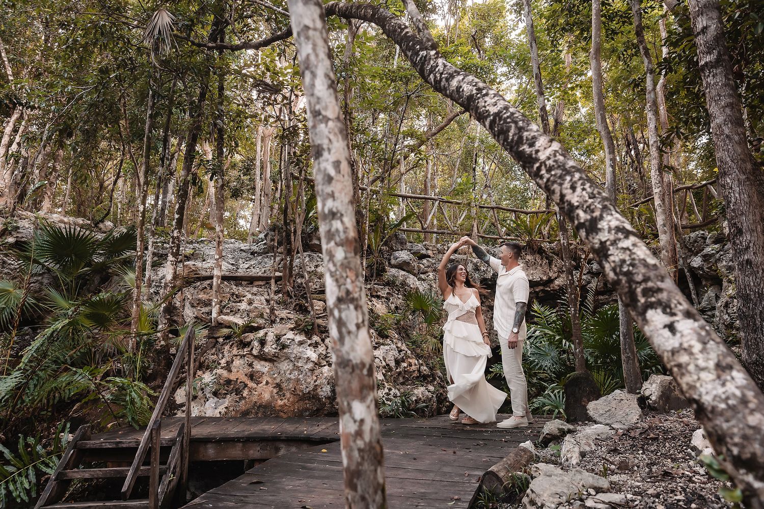 Two people walk along a wooden pathway surrounded by birch trees in a forest.