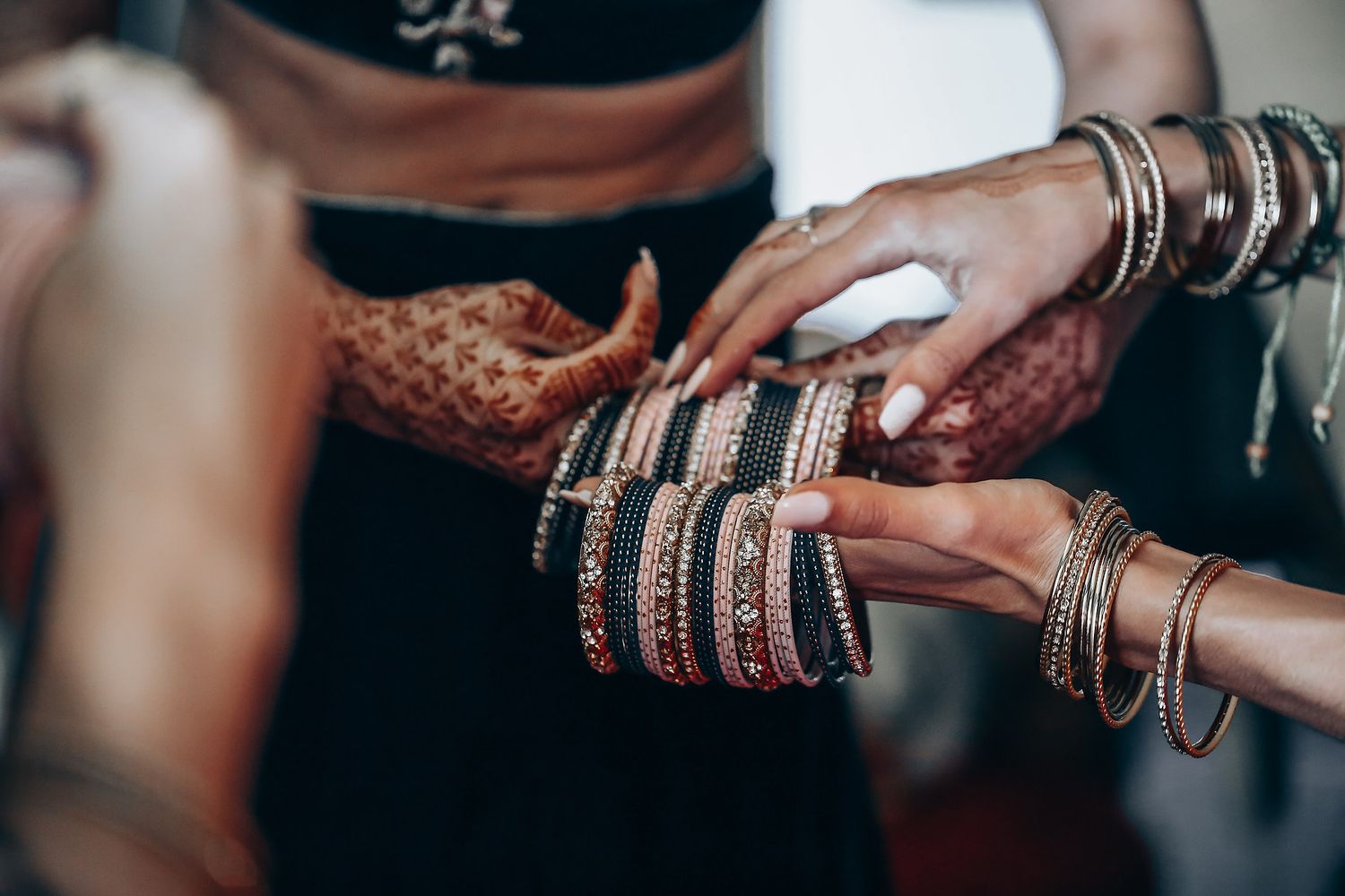 Hands adorned with intricate henna designs and bangles during a traditional Indian wedding ceremony.