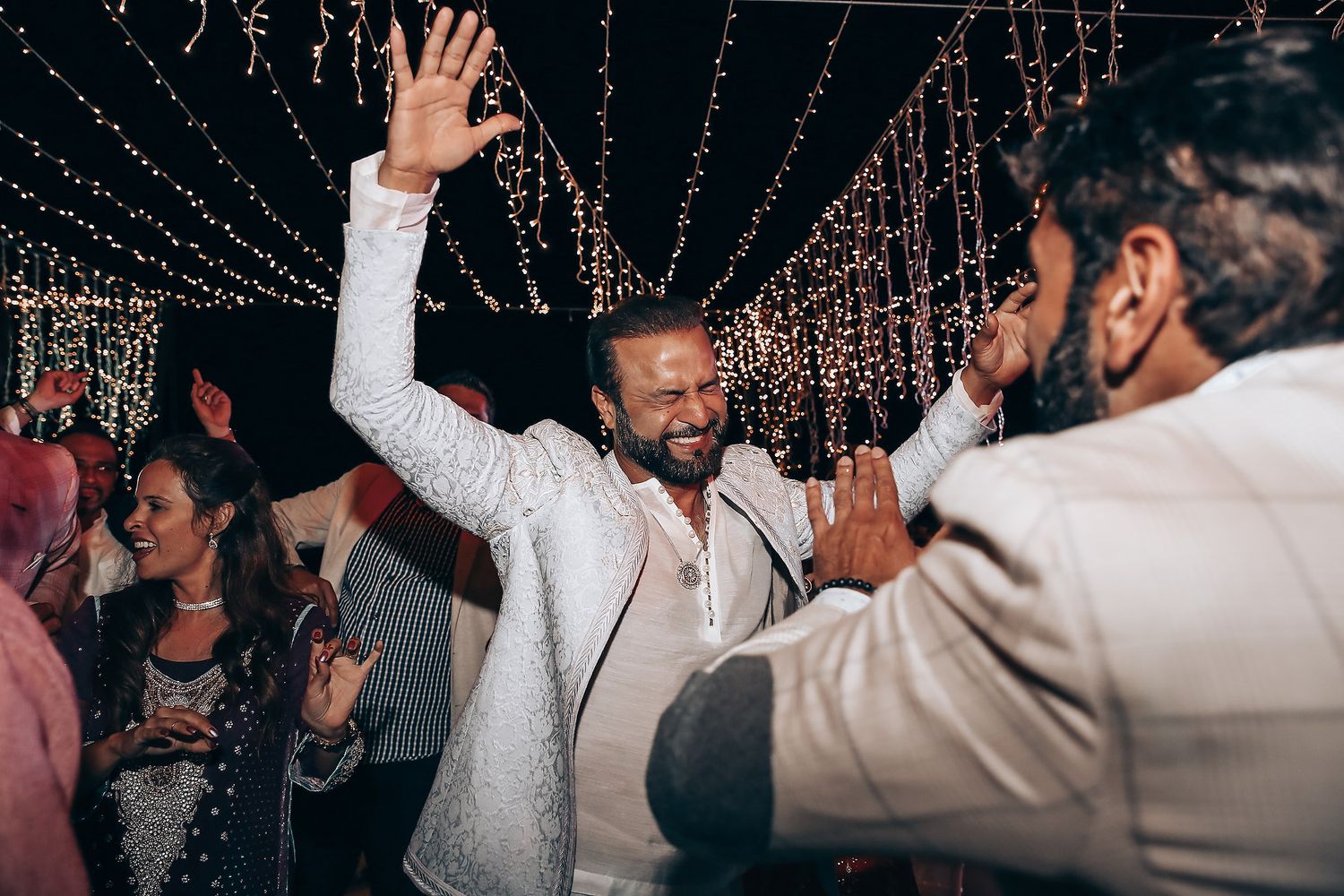 People dancing and celebrating at a nighttime wedding reception under twinkling string lights.