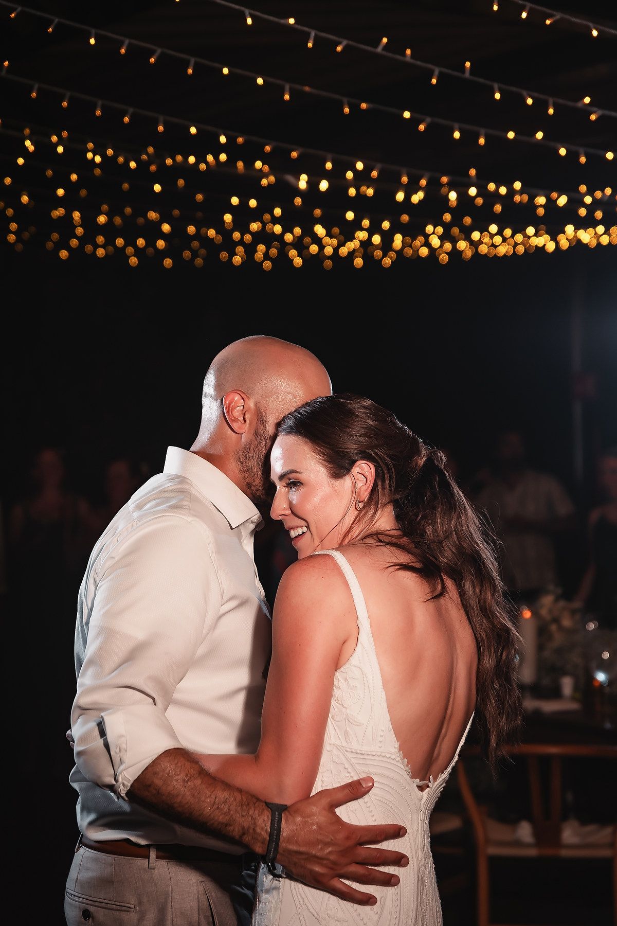 A romantic dance under twinkling string lights at an evening wedding reception.