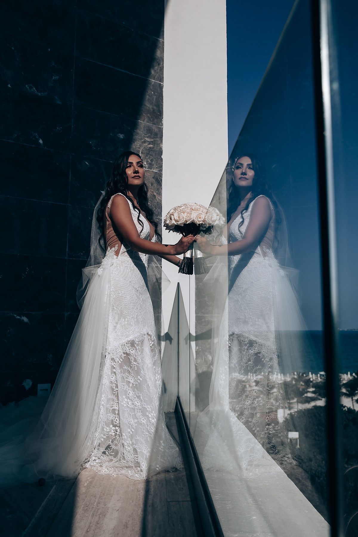 A bride in a white lace wedding gown is reflected in window glass creating an artistic double exposure effect.