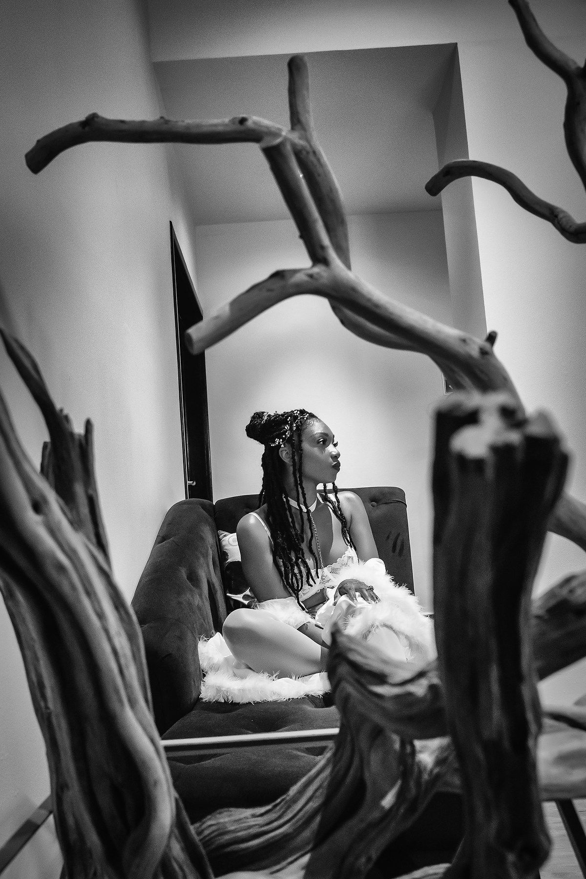 A black and white photo series showing a person reclining on a couch with dramatic driftwood pieces in the foreground.