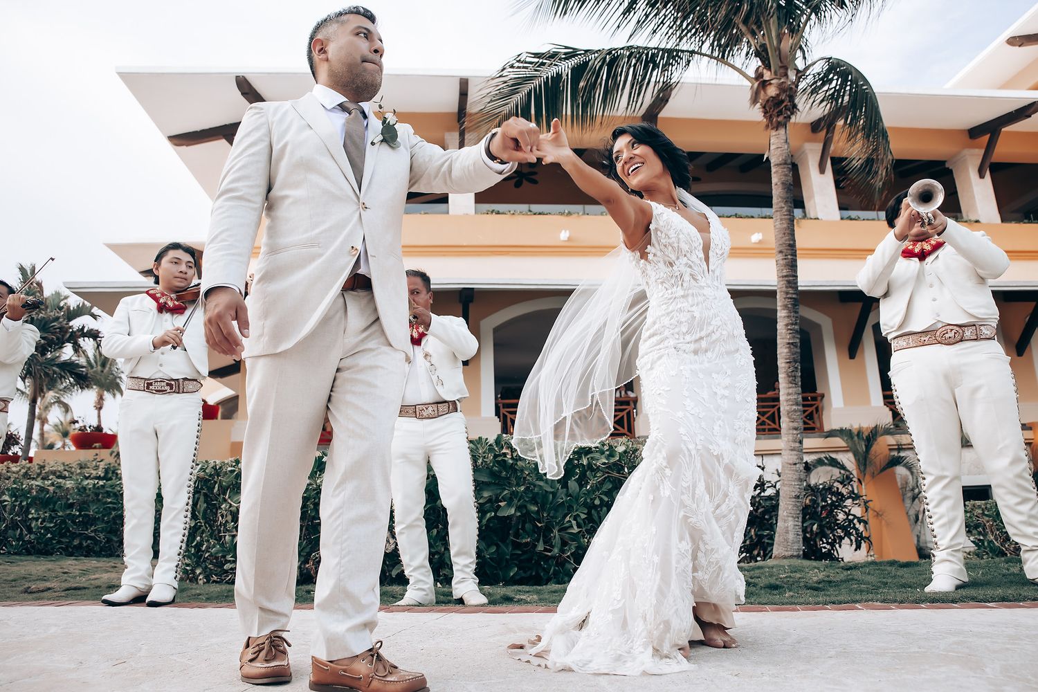 Wedding party members in all-white attire dancing and celebrating on a beachfront patio.