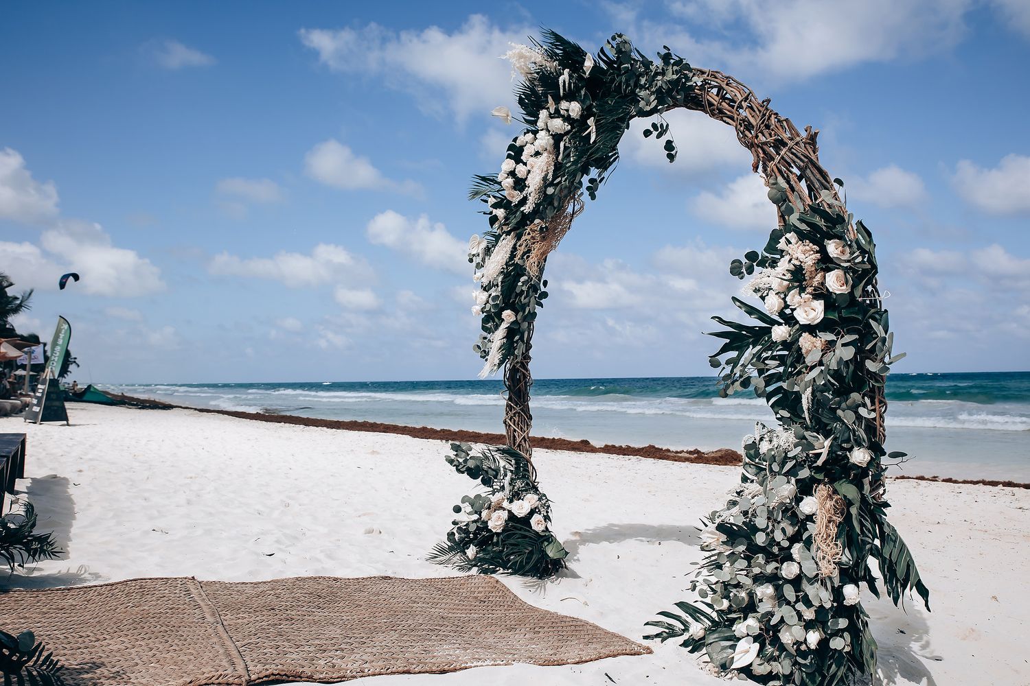 Floral wedding arch setup on a tropical beach with waves crashing in the background.